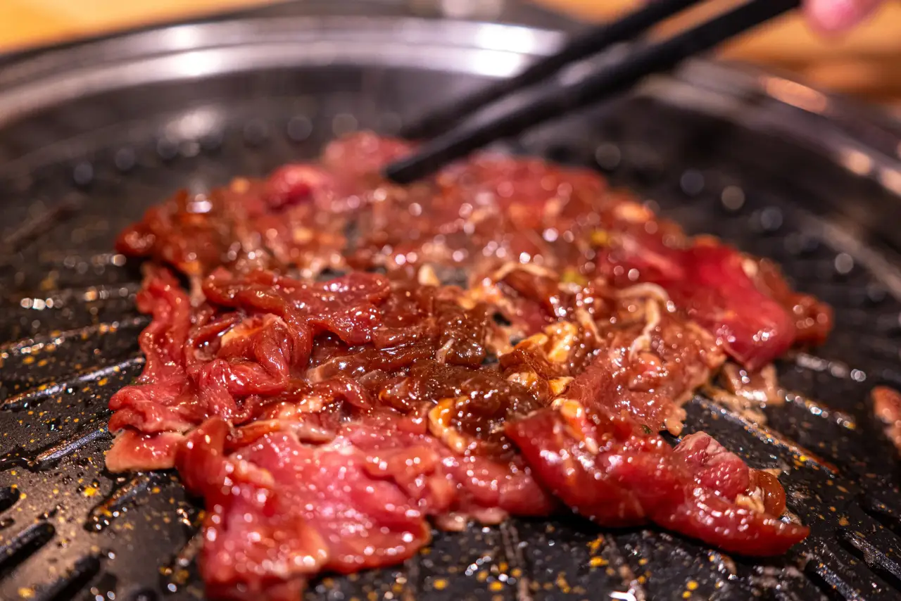 Mariniertes Rinderbulgogi brutzelt auf der schwarzen Grillplatte des Tischgrills und wird mit Stäbchen gewendet.