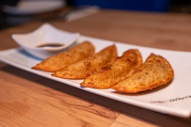 Vier goldbraun gebratene Mandu-Teigtaschen auf einem länglichen weißen Teller mit einem Schälchen Sojasauce.